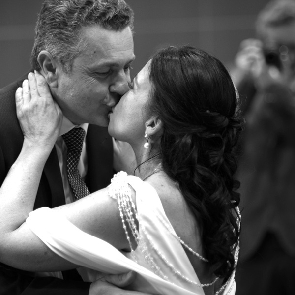 Bride and groom kiss after the wedding vows. In the background photographers capturing this image. The photo is in black and white.