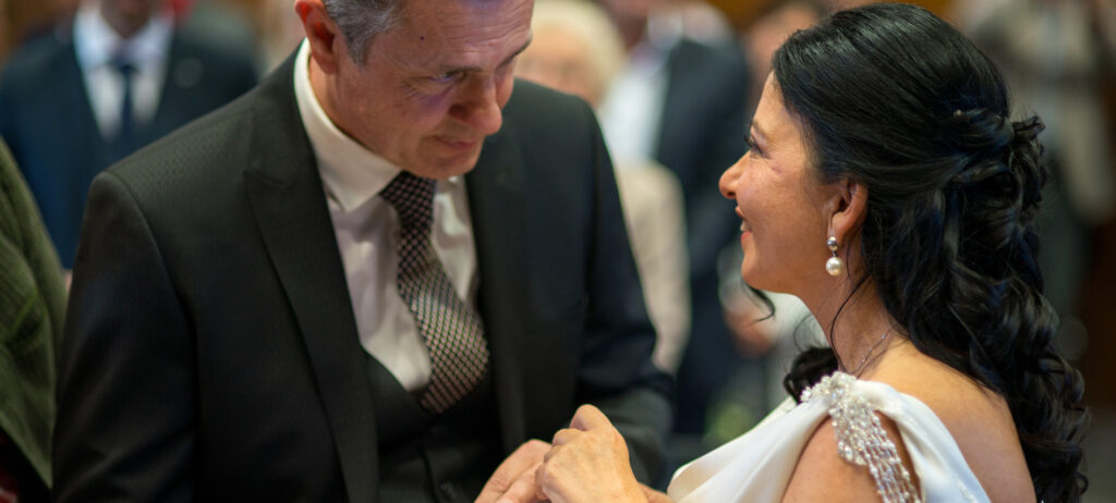 Ring exchange at the registry office. The groom slides the wedding ring over the ring finger of the bride. The couple looks at each other in love.