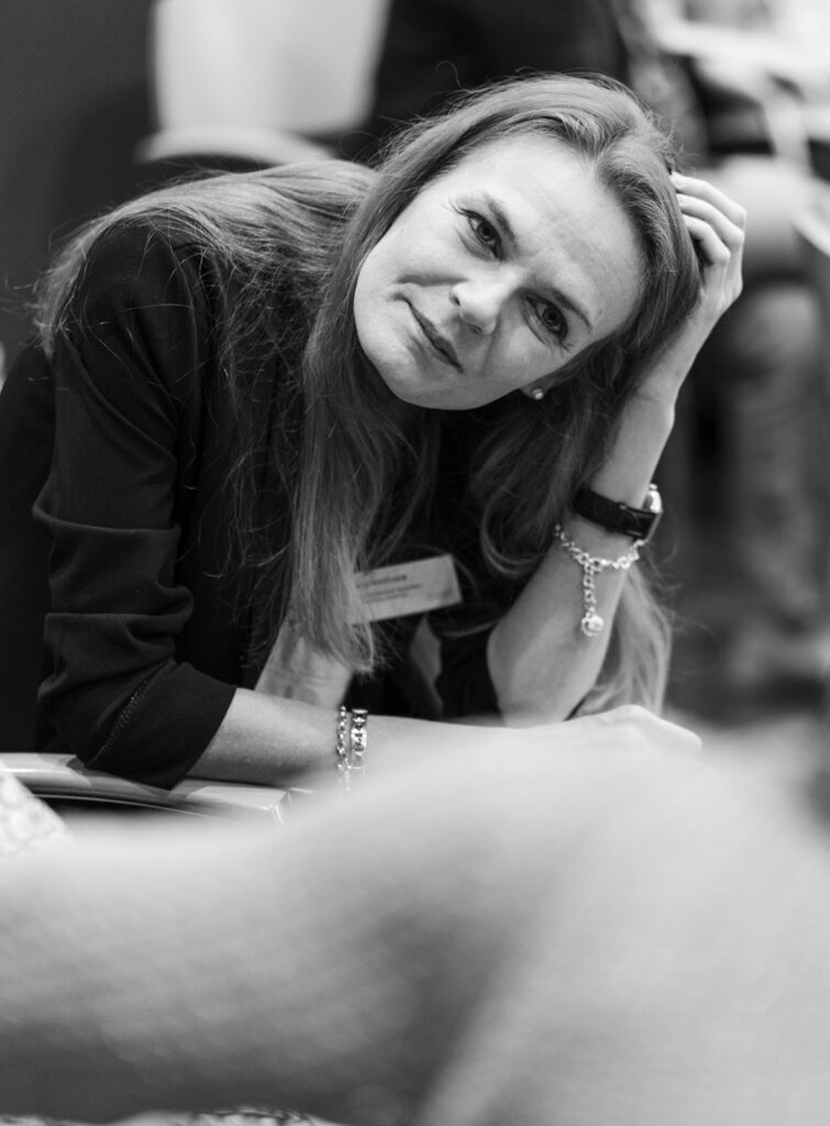 A pretty lady about 40 years old tilts her head to the side, puts her left hand to her hair and listens attentively to her counterpart.