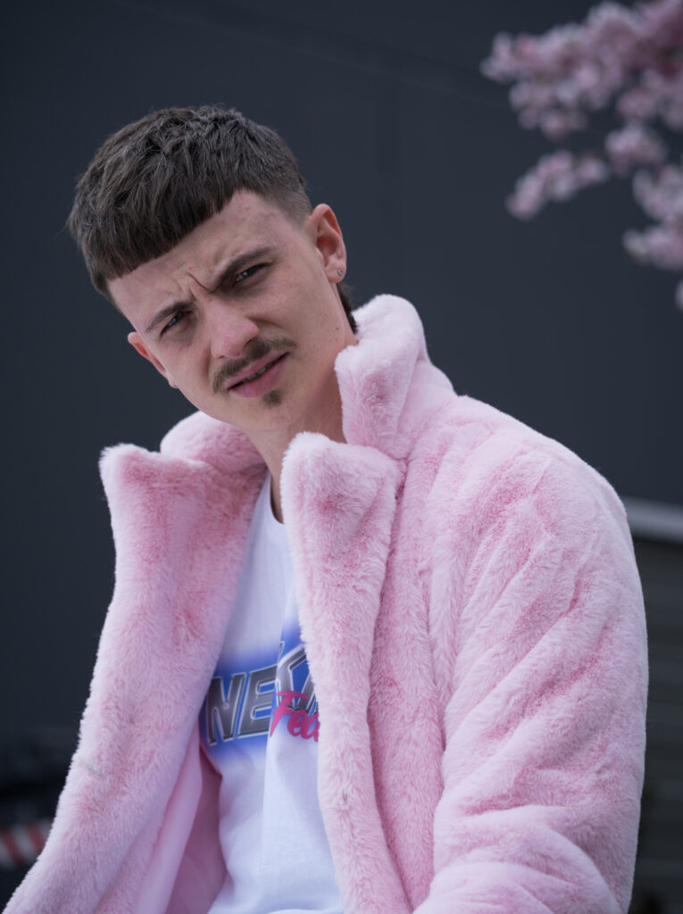 Portrait view of the rapper in the plush jacket. He looks skeptically into the camera.